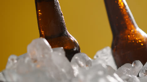 Nahaufnahme-Von-Glasflaschen-Mit-Kaltem-Bier-Oder-Alkoholfreien-Getränken,-Die-In-Einem-Mit-Eis-Gefüllten-Eimer-Vor-Gelbem-Hintergrund-Kühlen-1